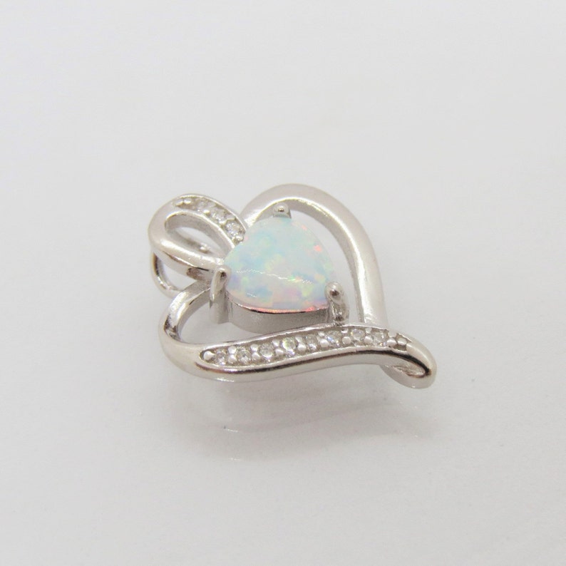 May include: A silver heart-shaped pendant with a white opal gemstone in the center. The pendant is accented with small clear stones around the edge.