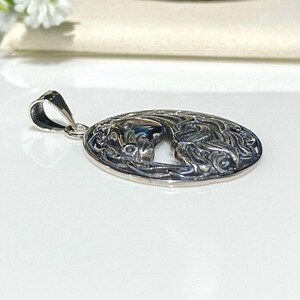 May include: Silver pendant with an oval design featuring a detailed, intricate Celtic knot pattern. The pendant has a cutout in the center, revealing a stylized horse head.