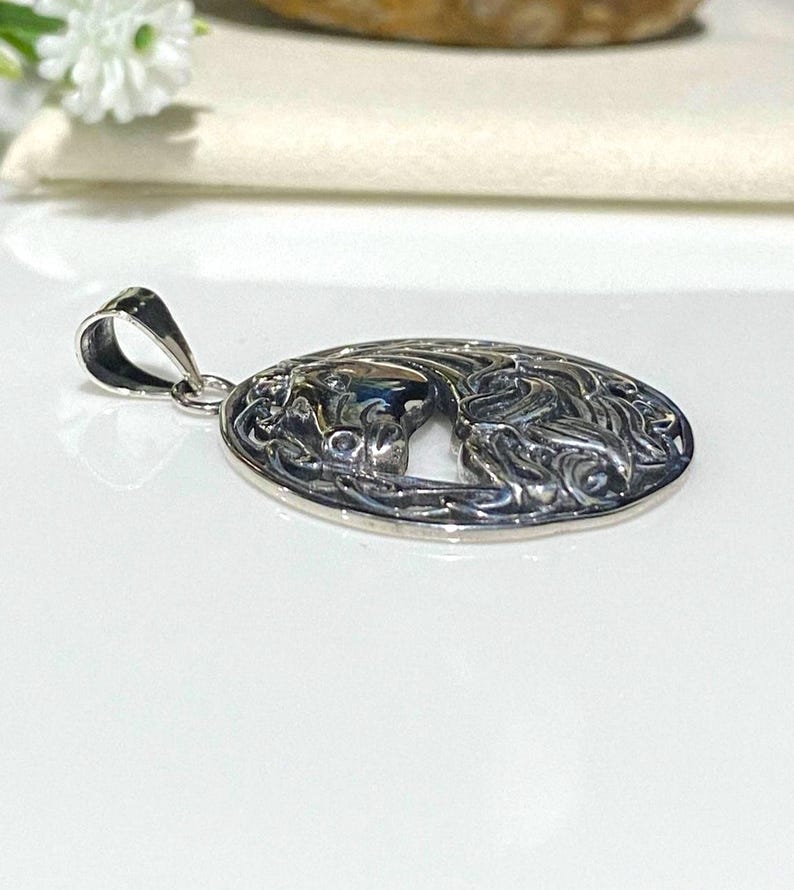May include: Silver pendant with an oval design featuring a detailed, intricate Celtic knot pattern. The pendant has a cutout in the center, revealing a stylized horse head.