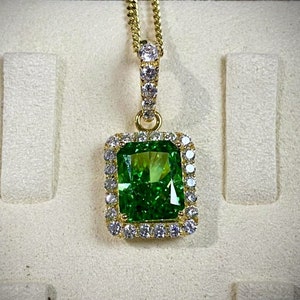 May include: A gold pendant necklace with a large, emerald green gemstone surrounded by smaller, clear gemstones.