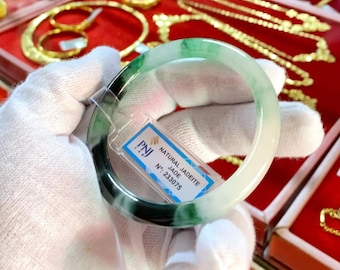 May include: A green jadeite bangle bracelet with a white and green swirl pattern. The bracelet is labeled "Natural Jadeite Jade" and "PNJ" with the number "233075".