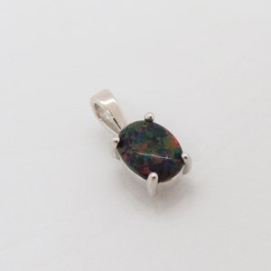 Puede incluir: Un colgante de plata con una piedra preciosa de &oacute;palo negro. El &oacute;palo tiene una base oscura con destellos de verde, rojo y azul.