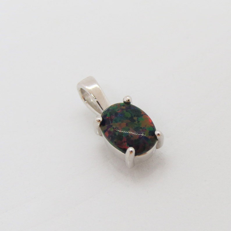 Puede incluir: Un colgante de plata con una piedra preciosa de &oacute;palo negro. El &oacute;palo tiene una base oscura con destellos de verde, rojo y azul.