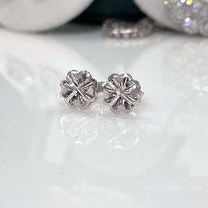Puede incluir: Un par de pendientes de plata. Cada pendiente presenta un dise&ntilde;o floral con m&uacute;ltiples p&eacute;talos y un centro detallado. Los pendientes est&aacute;n sobre un fondo blanco, resaltando su intrincado dise&ntilde;o y brillo met&aacute;lico.