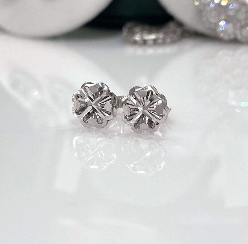 Puede incluir: Un par de pendientes de plata. Cada pendiente presenta un dise&ntilde;o floral con m&uacute;ltiples p&eacute;talos y un centro detallado. Los pendientes est&aacute;n sobre un fondo blanco, resaltando su intrincado dise&ntilde;o y brillo met&aacute;lico.