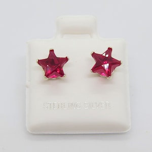 May include: A pair of sterling silver star-shaped stud earrings with red gemstones. The earrings are displayed on a white card with the text "Sterling Silver".