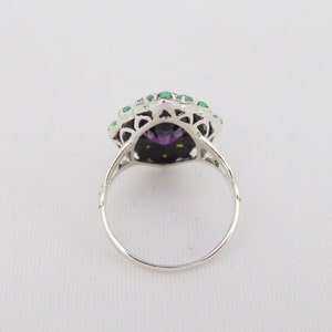 May include: A silver ring with a large purple gemstone surrounded by smaller green gemstones.