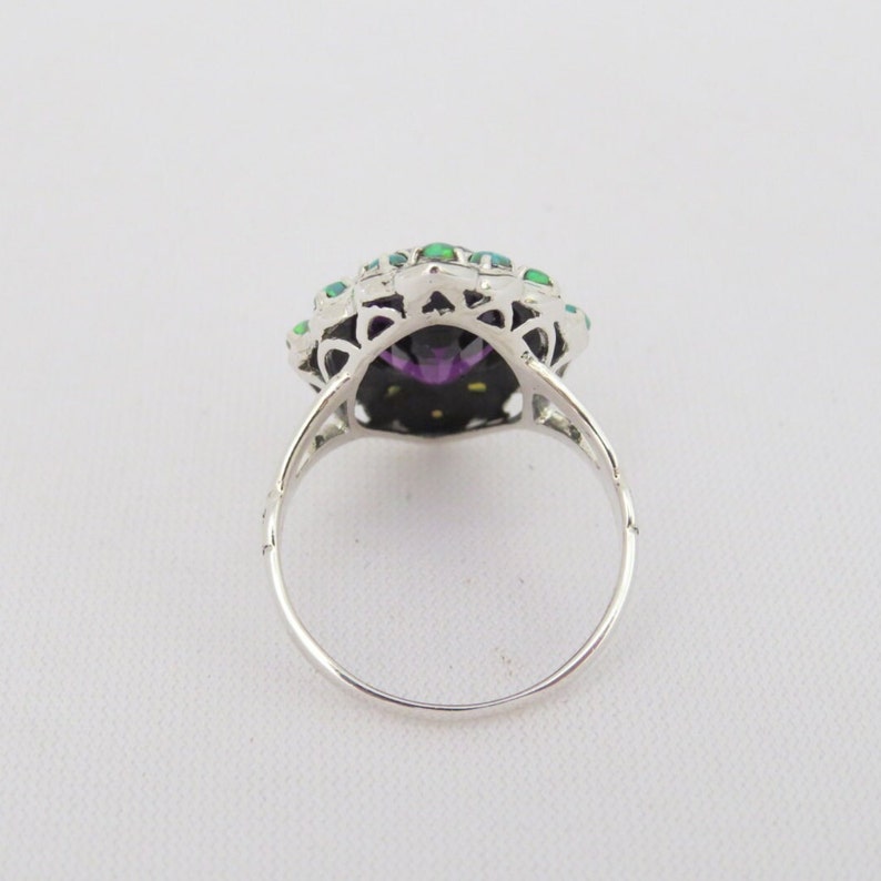 May include: A silver ring with a large purple gemstone surrounded by smaller green gemstones.