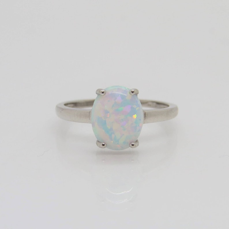 Peut inclure: Une bague en argent avec une pierre pr&eacute;cieuse en opale blanche. L'opale pr&eacute;sente un &eacute;clat iris&eacute; bleu clair et rose.