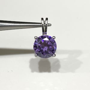 May include: A silver pendant with a round, purple gemstone.