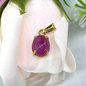 Puede incluir: Un colgante de oro con una piedra preciosa ovalada rosa engastada en un engaste de oro.
