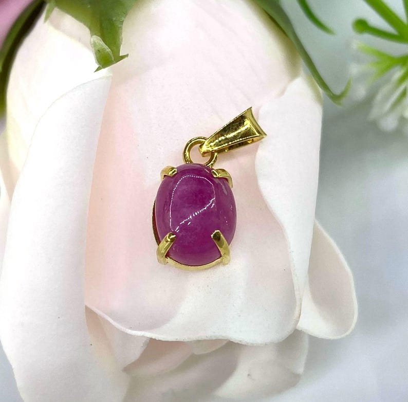 Puede incluir: Un colgante de oro con una piedra preciosa ovalada rosa engastada en un engaste de oro.
