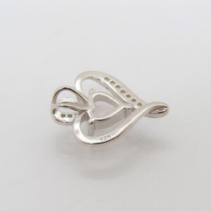 May include: A silver heart-shaped pendant with a smaller heart in the center. The pendant is set with small clear stones around the edge and has a 925 stamp on the back.