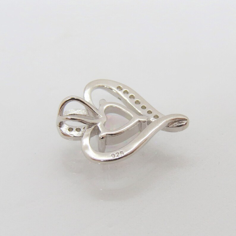 May include: A silver heart-shaped pendant with a smaller heart in the center. The pendant is set with small clear stones around the edge and has a 925 stamp on the back.