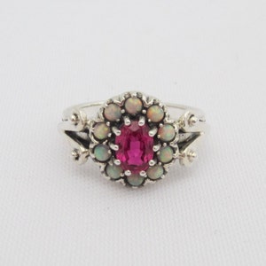 Puede incluir: Un anillo de plata con una piedra ovalada rosa rodeada por un halo de ópalos blancos.