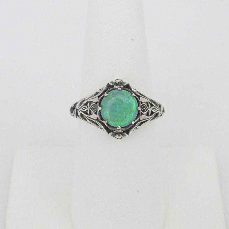 Pode incluir: Um anel de prata com um design ornamentado que apresenta uma gema de opala verde.