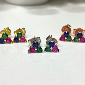 May include: Three pairs of small triangle-shaped earrings with three gemstones each. The earrings are in gold, rose gold, and silver. The gemstones are blue, green, and pink.
