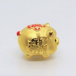 May include: A small gold piggy bank with red and white accents. The piggy bank has Chinese characters on the side.