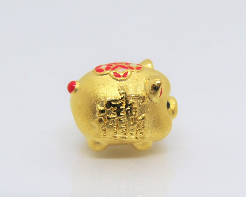 May include: A small gold piggy bank with red and white accents. The piggy bank has Chinese characters on the side.