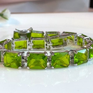 May include: A silver bracelet featuring rectangular, lime green gemstones. The gemstones are set in a silver metal frame, creating a continuous chain. The bracelet is designed with a clasp for secure wear.