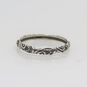 May include: A silver ring with a delicate, intricate design featuring swirls and dots. The ring is thin and has a polished finish.