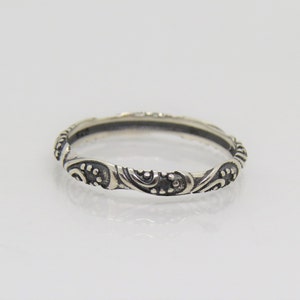 May include: A silver band ring with a delicate, intricate design of swirls and dots.