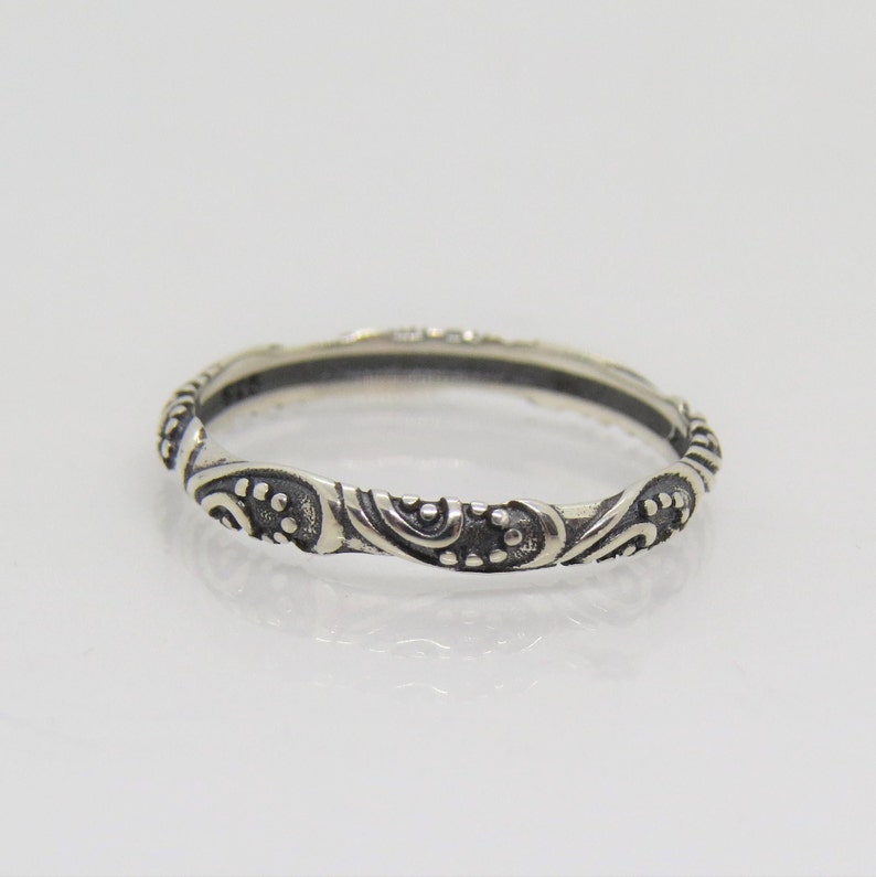 May include: A silver band ring with a delicate, intricate design of swirls and dots.