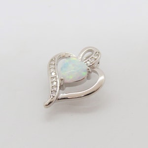 May include: A silver heart-shaped pendant with a white opal gemstone in the center. The pendant is accented with small clear cubic zirconia stones.