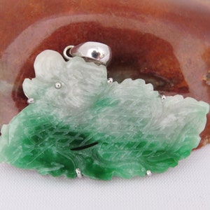 Pode incluir: Um pingente de jade verde e branco esculpido em forma de folha com detalhes prateados.