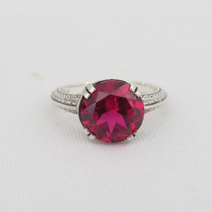 May include: A silver ring with a large, round, red gemstone set in a filigree design.