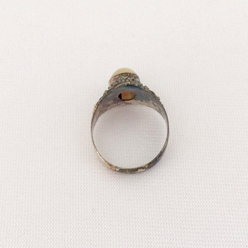 May include: A silver ring with a white pearl set in a decorative bezel. The ring has a simple band.