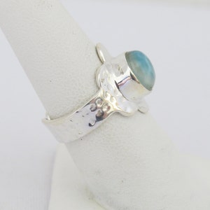 May include: A silver ring with a textured band and a light blue gemstone set in a silver bezel.