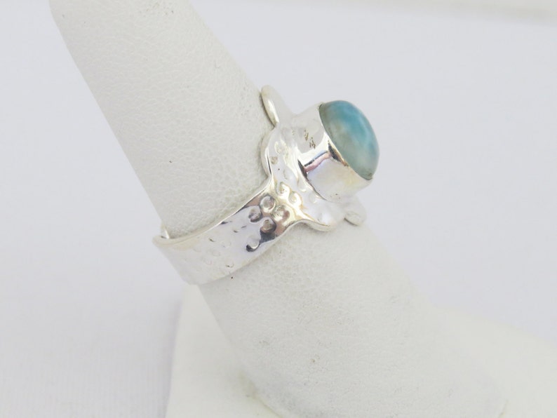 May include: A silver ring with a textured band and a light blue gemstone set in a silver bezel.