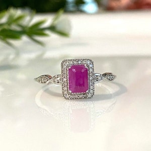 May include: A silver ring with a pink rectangular gemstone surrounded by smaller diamonds. The ring has a delicate, twisted band.