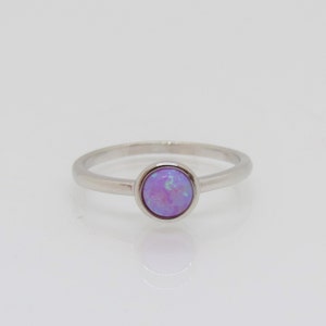 Puede incluir: Un anillo de plata con una piedra de &oacute;palo redonda y de color p&uacute;rpura claro. El &oacute;palo tiene una mezcla de colores, incluyendo azul claro y verde. La banda del anillo es delgada y de metal plateado.