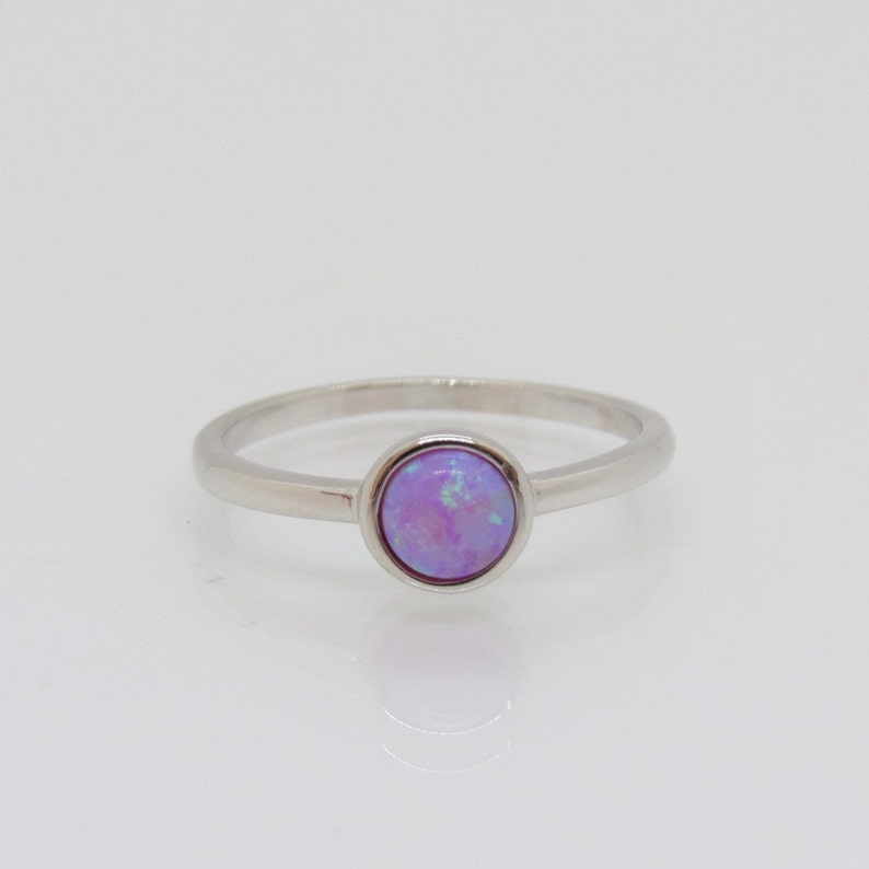 Puede incluir: Un anillo de plata con una piedra de &oacute;palo redonda y de color p&uacute;rpura claro. El &oacute;palo tiene una mezcla de colores, incluyendo azul claro y verde. La banda del anillo es delgada y de metal plateado.