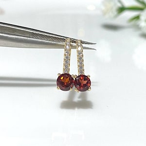 May include: A pair of gold earrings with a red gemstone and a row of clear stones on each earring.