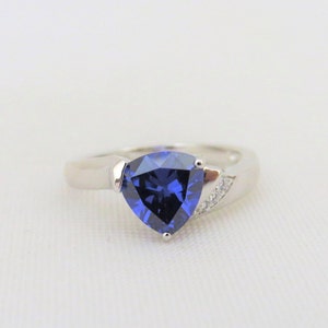 May include: A silver ring featuring a triangular blue gemstone and smaller clear gemstones on the band.