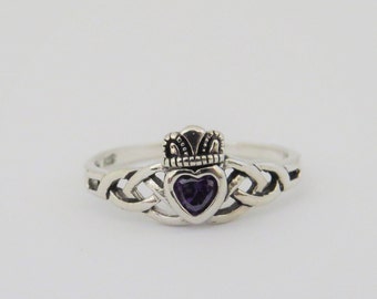 May include: A silver ring with a Celtic knot design and a purple heart-shaped gemstone in the center. The ring has a crown on top of the heart.