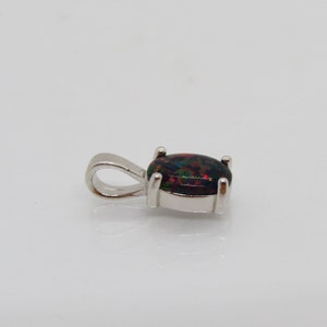 Puede incluir: Un colgante de plata con una piedra preciosa de &oacute;palo negro. El &oacute;palo tiene una base oscura con destellos de rojo, verde y azul.
