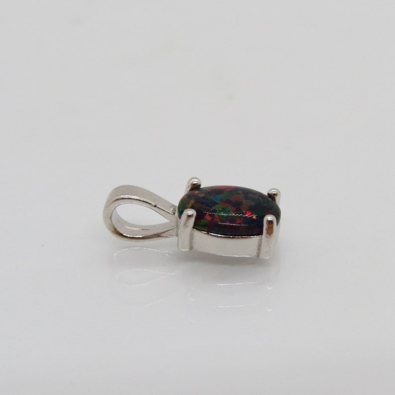 Puede incluir: Un colgante de plata con una piedra preciosa de &oacute;palo negro. El &oacute;palo tiene una base oscura con destellos de rojo, verde y azul.