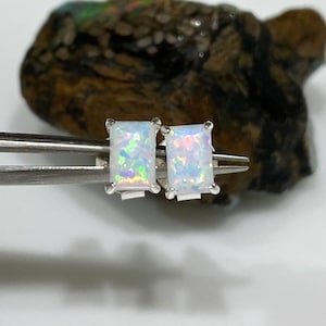 May include: A pair of silver stud earrings with rectangular white opal gemstones. The opals have a rainbow iridescent sheen.