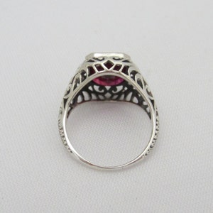 May include: A silver ring with a filigree design and a pink gemstone in the center.