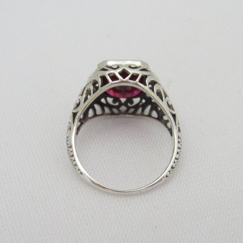 May include: A silver ring with a filigree design and a pink gemstone in the center.