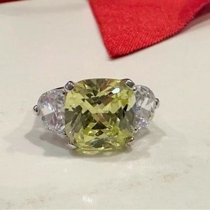May include: A silver ring with a large, cushion-cut, yellow gemstone surrounded by two smaller, round, clear gemstones.