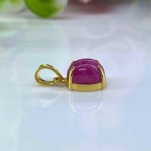 Puede incluir: Un colgante de oro con una piedra preciosa rosa engastada en un engaste de bisel. El colgante tiene un aro para sujetarlo a una cadena.