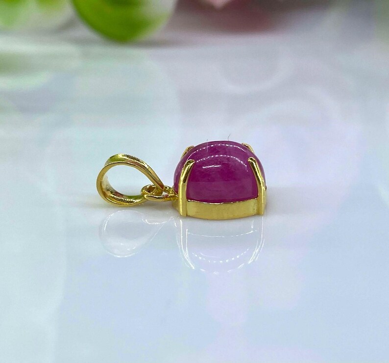 Puede incluir: Un colgante de oro con una piedra preciosa rosa engastada en un engaste de bisel. El colgante tiene un aro para sujetarlo a una cadena.