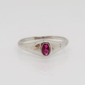 May include: A silver ring with a single oval-shaped ruby gemstone set in the center.