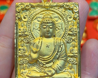 May include: A gold pendant featuring a detailed depiction of Buddha in a seated meditation pose. The pendant is rectangular with an ornate border and intricate details throughout.