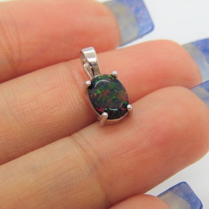 Puede incluir: Un colgante de plata con una piedra preciosa de &oacute;palo negro. El &oacute;palo tiene destellos de color verde, rojo y marr&oacute;n.